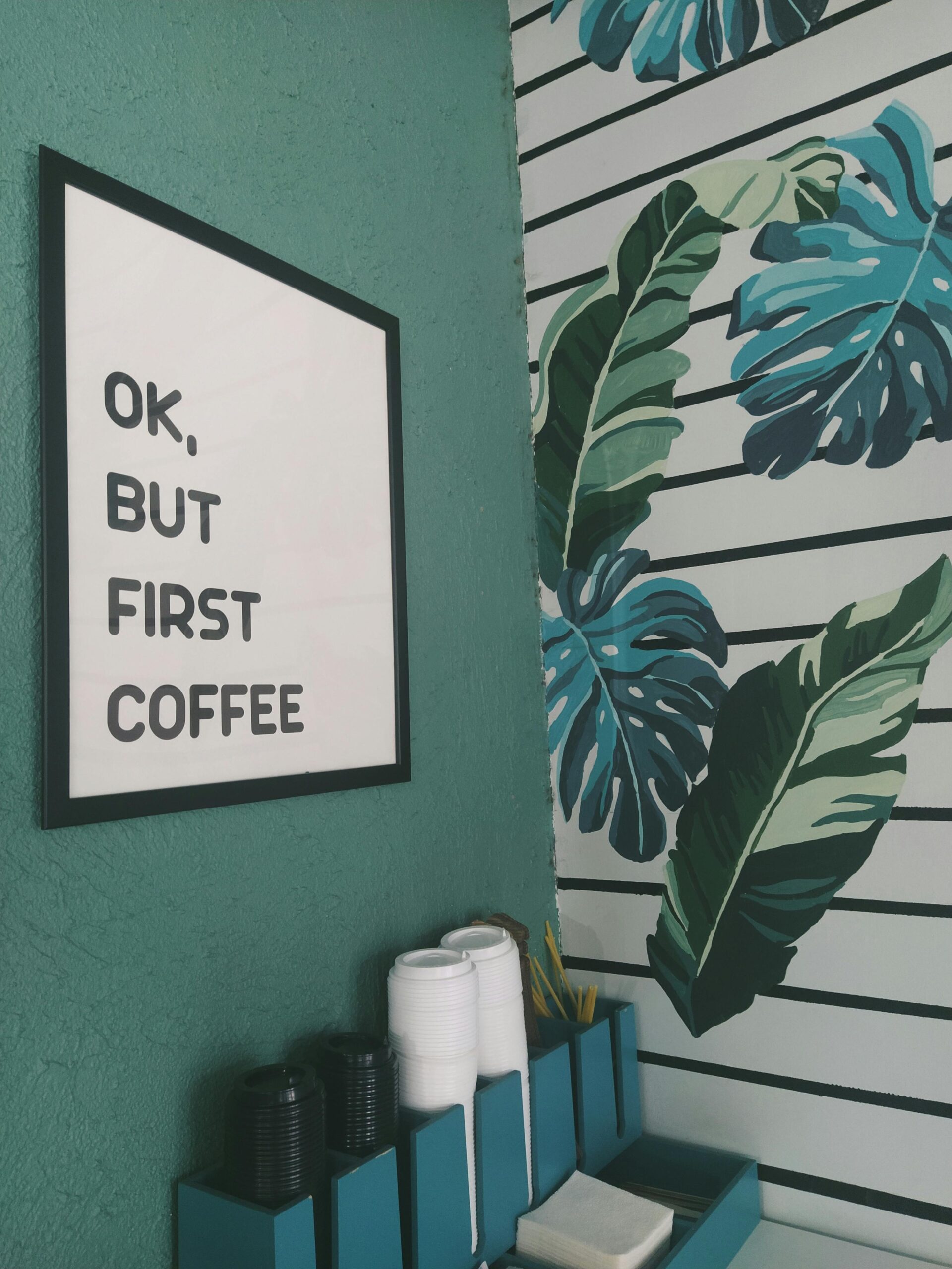 A stylish coffee corner featuring tropical leaf wallpaper and a coffee-themed sign.